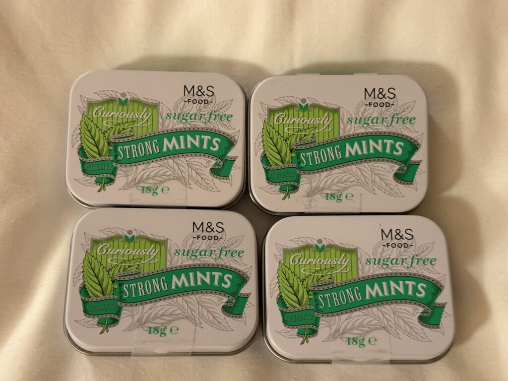Four tins of Marks & Spencer Curiously Strong Mints sugar free arranged in a square