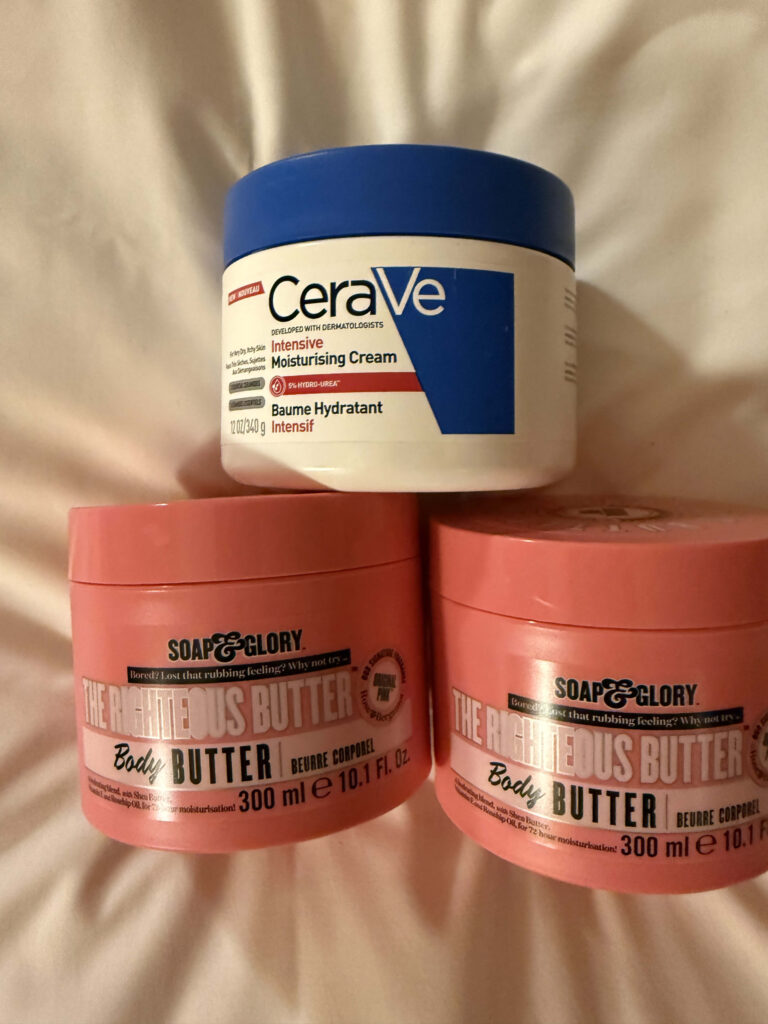 白いシーツの上に積み重ねられた、CeraVeのモイスチャライジングクリームと2つのSoap & Gloryのザ・ライチャス・バター