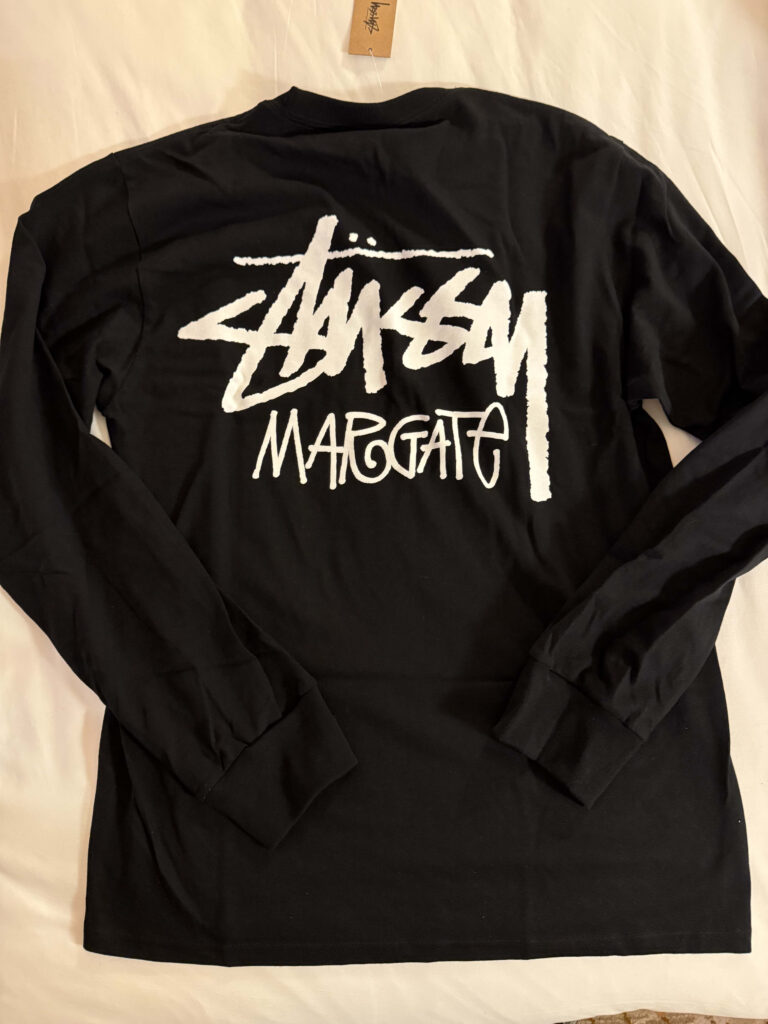 The back of a black long-sleeved T-shirt. The Stüssy logo and the word 'MARGATE' are largely printed in white in the center.