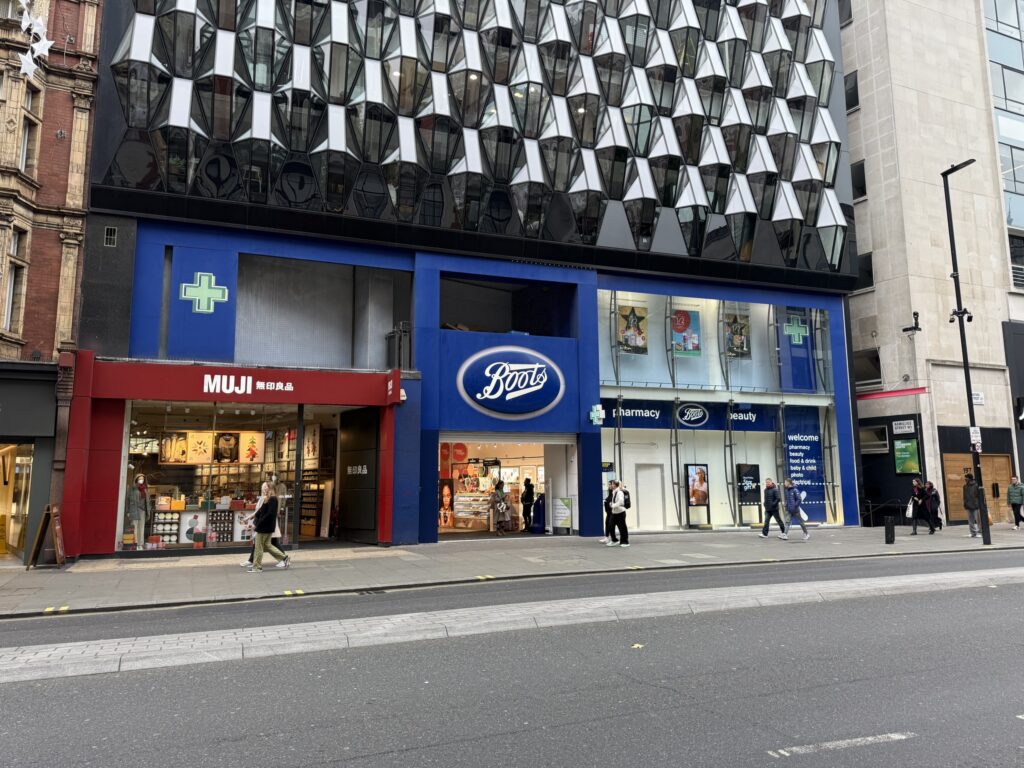 Exterior of Boots and MUJI stores on Oxford Street in London beneath a geometric faceted building facade