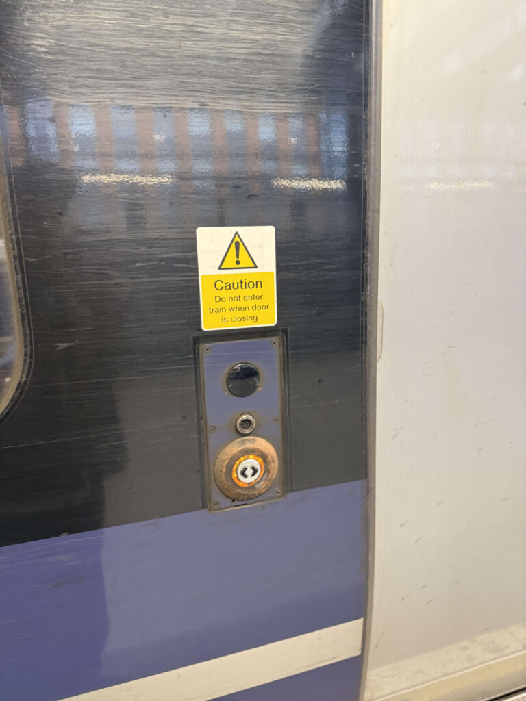 電車のドアにある、黄色い注意書きのステッカーと、ドアを開けるための光るボタンのクローズアップ写真。