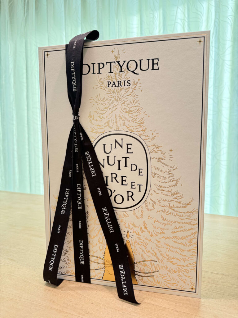 Diptyque's holiday collection packaging with a black ribbon tied around it, placed on a wooden table.