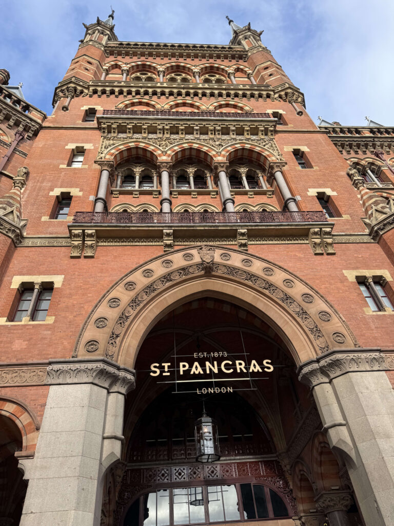 ロンドンのセント・パンクラス駅の壮麗な赤レンガの建物を下から見上げた写真。ゴシック・リヴァイヴァル建築の正面玄関のアーチには「ST PANCRAS」のサインが掲げられている。