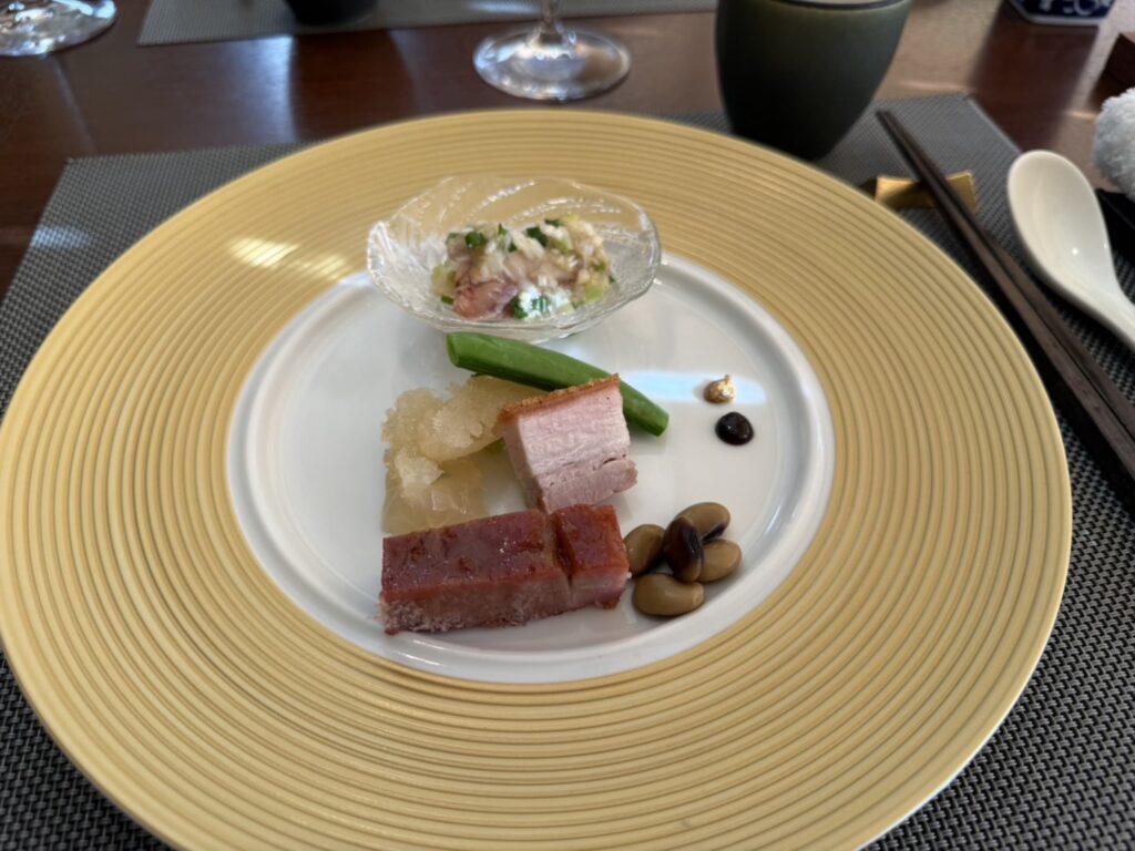 An assortment of Chinese-style appetizers, including char siu and crispy-skin roasted pork belly, beautifully arranged on a yellow-rimmed plate.