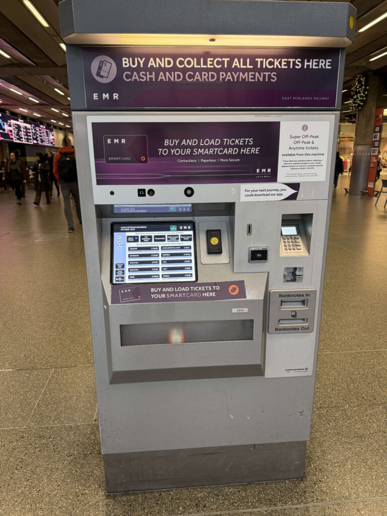 A front view of an East Midlands Railway (EMR) ticket vending machine in a train station, featuring a touchscreen, card payment terminal, and cash slots.