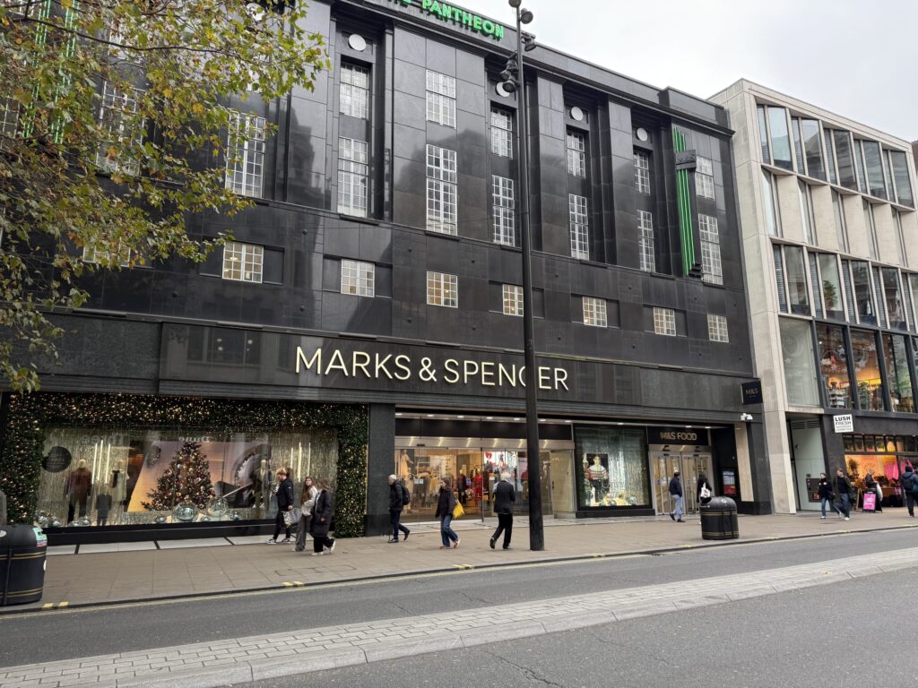 ロンドン・ソーホーにあるMarks & Spencerの店舗外観。黒い石造りの建物に金色のロゴ、ショーウィンドウにはクリスマスの装飾が施されている。