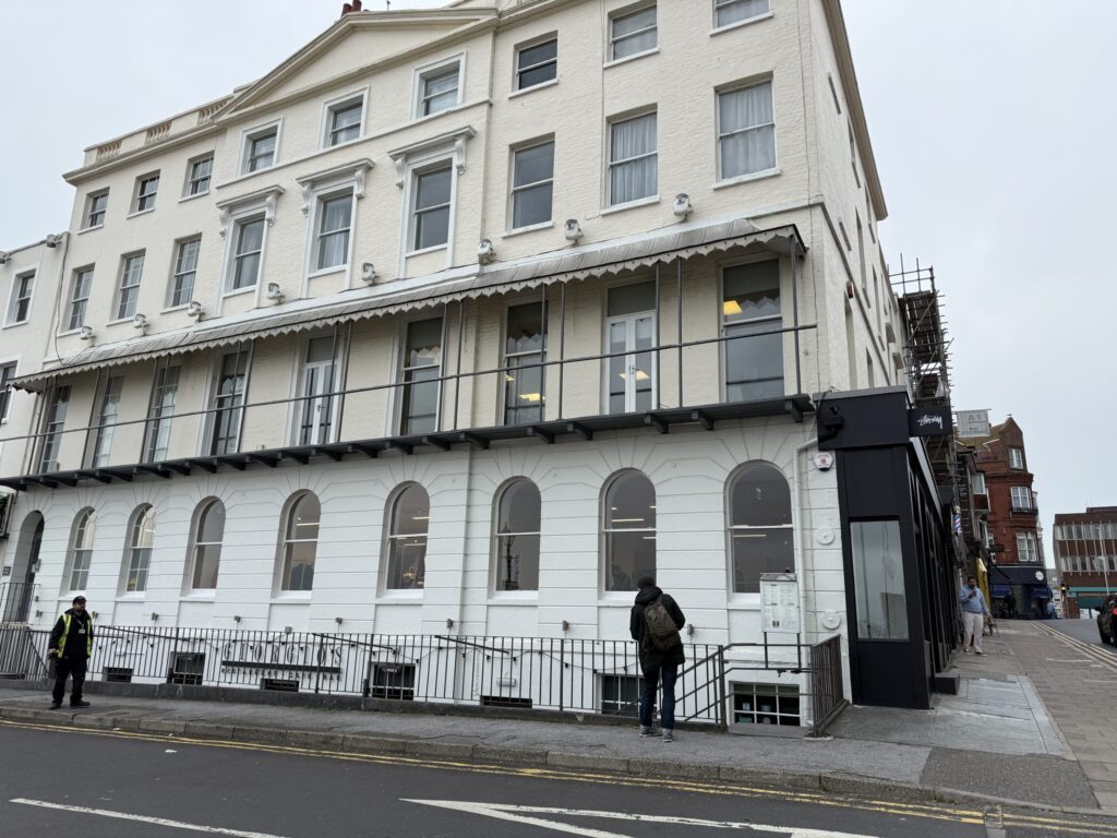 イギリスのマーゲイトにあるStüssyストア。オフホワイトのクラシカルな建物の角にあり、曇り空の下、人々が歩道を歩いている。