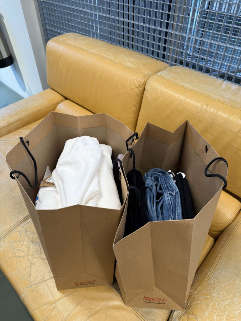 黄色い革のソファの上に置かれた、購入した服が入っている2つの茶色いショッピングバッグ。