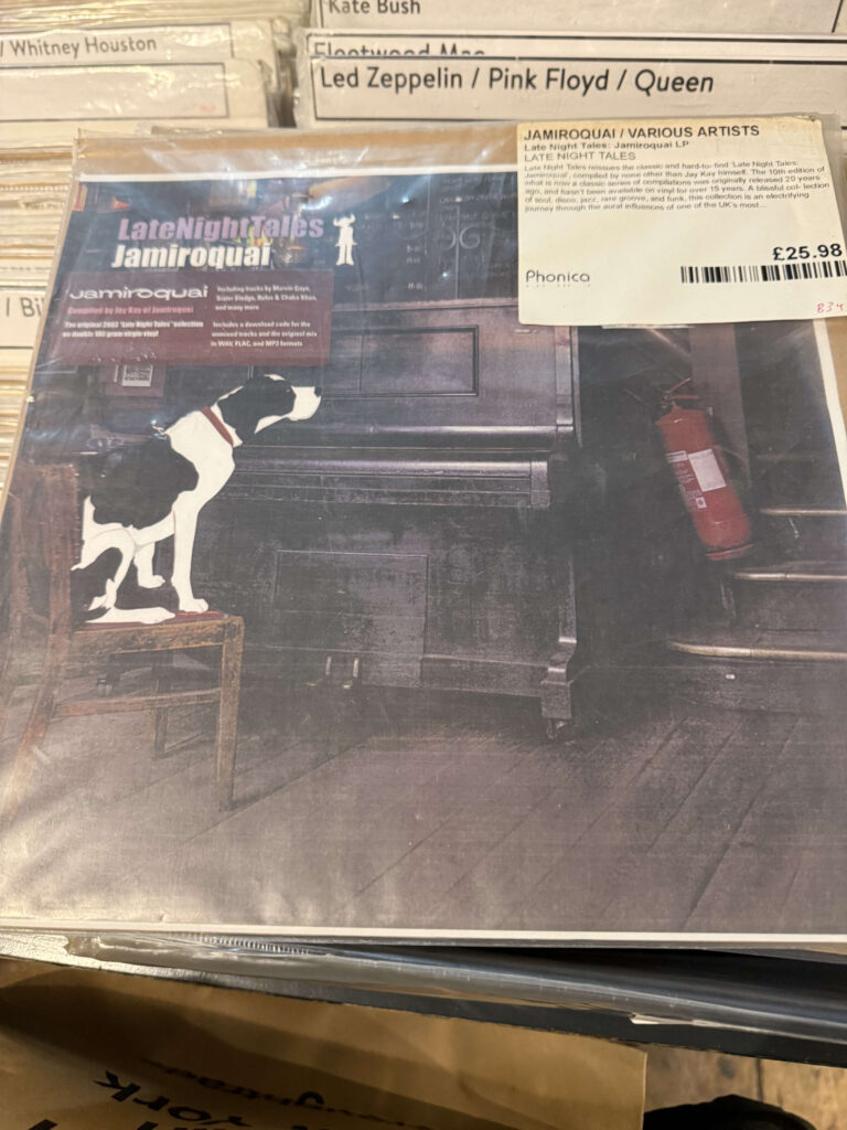 The vinyl record of Jamiroquai's compilation album 'Late Night Tales' in a record store. The cover art features a dog standing on a chair next to a piano.
