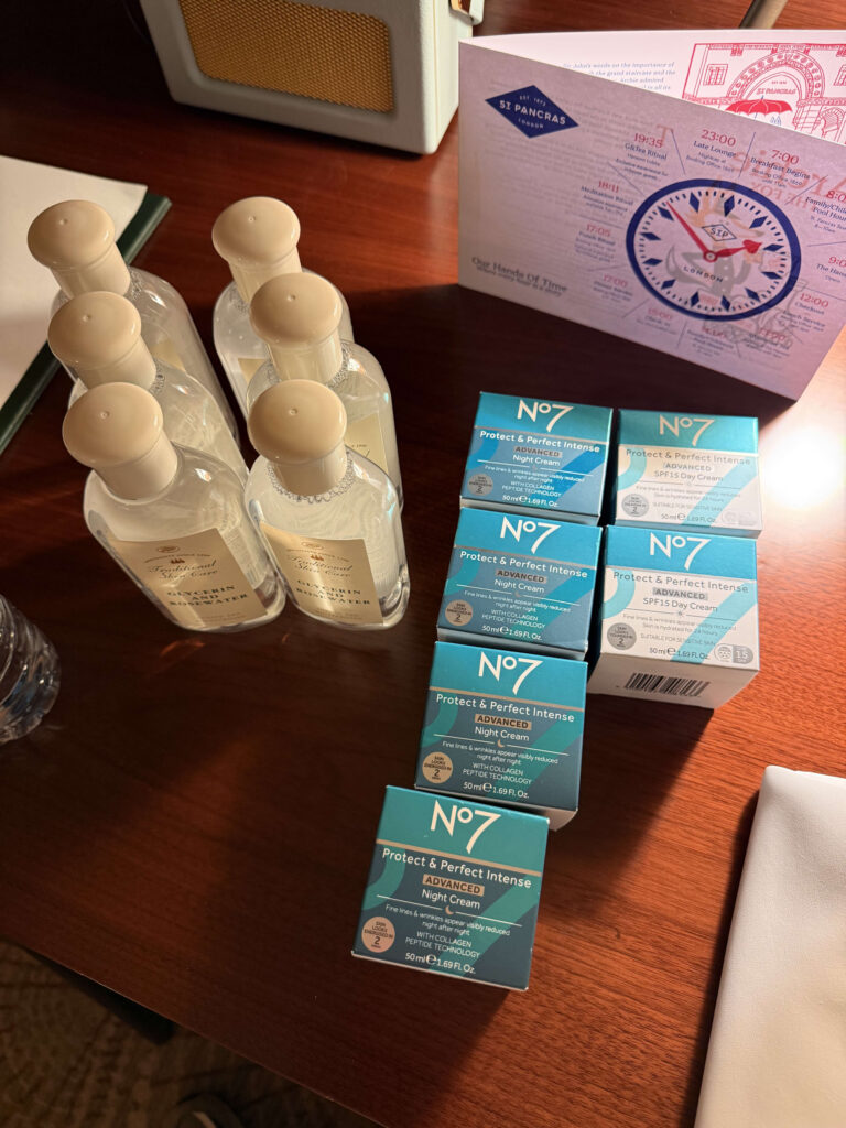 Six bottles of Glycerin and Rosewater and a stack of No7 Protect & Perfect Intense Advanced day and night cream boxes on a wooden table