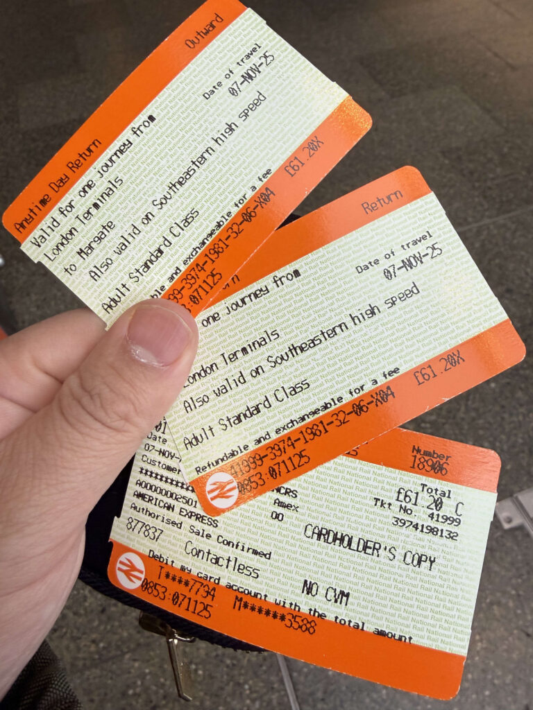 A hand holding orange National Rail return train tickets and a receipt for a journey in the UK.