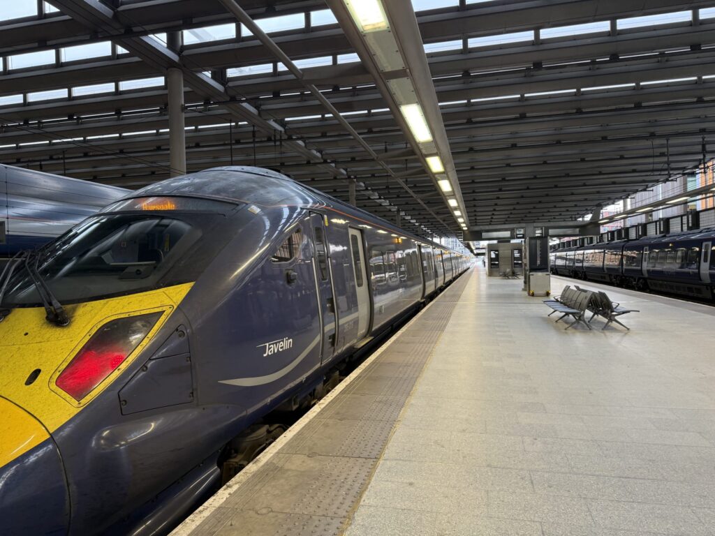 A Southeastern Javelin high-speed train at a station platform. The blue train has a yellow front and is waiting under a modern roof.