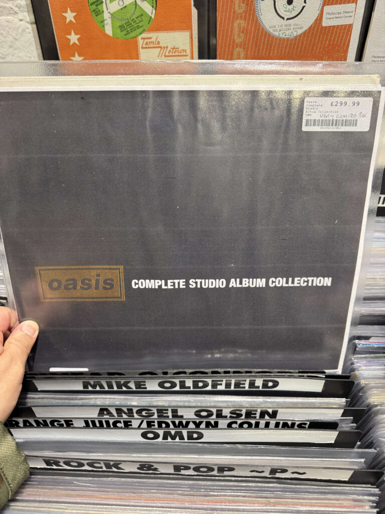A person's hand holding the Oasis 'Complete Studio Album Collection' vinyl box set in a record store.