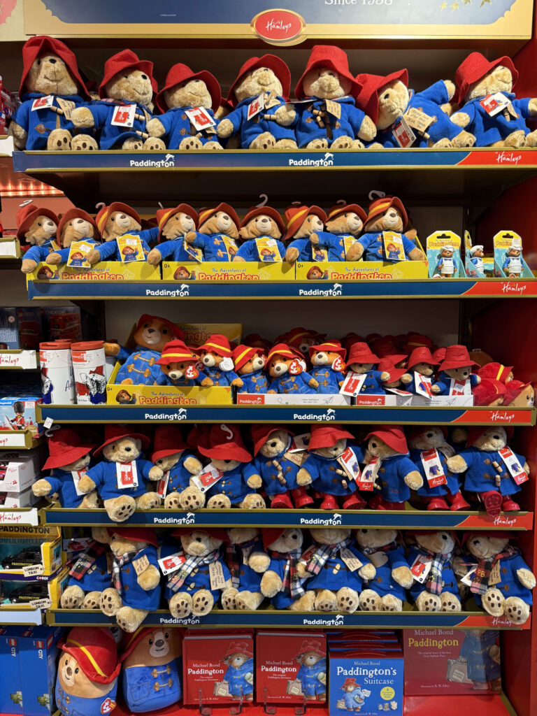 Shelves in a toy store are densely packed with Paddington Bear plush toys, all wearing their signature red hats and blue duffel coats.