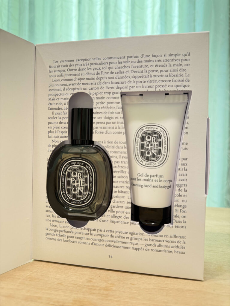 A Diptyque Orphéon gift set in a book-shaped box. Inside, a bottle of eau de parfum and a tube of hand & body wash gel are displayed side by side.