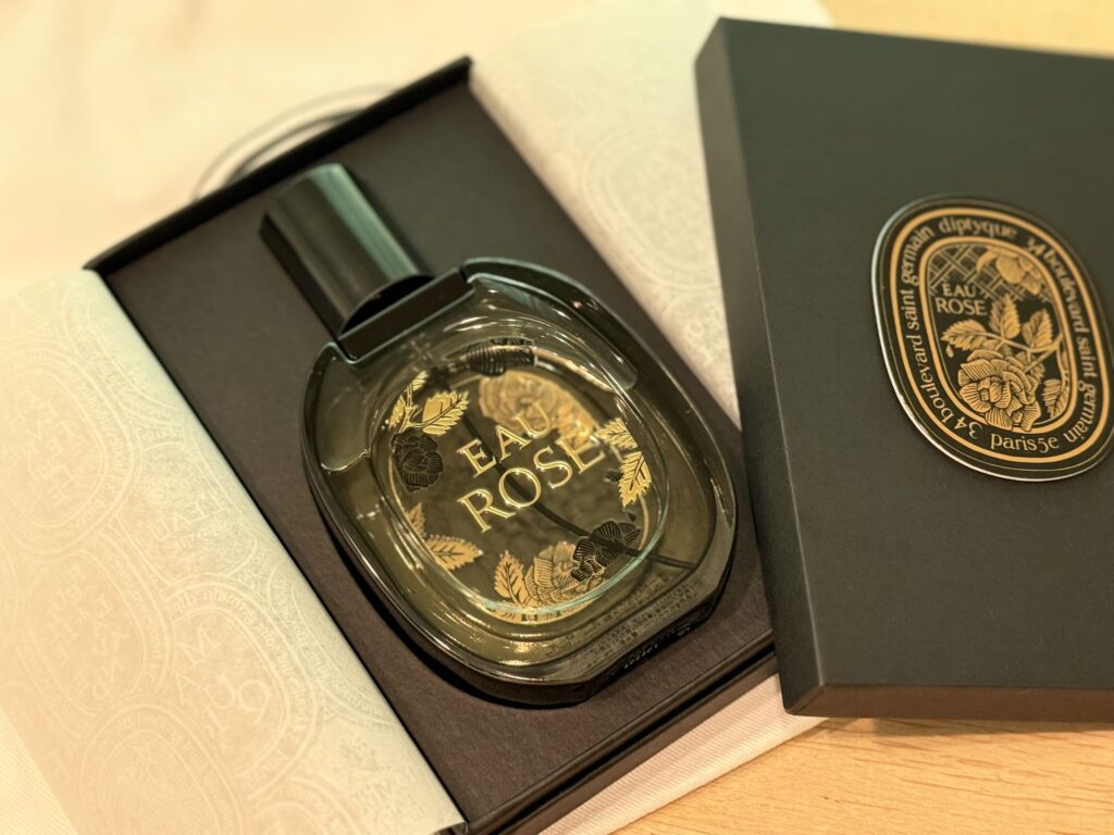 黒い箱の中に置かれたdiptyqueの香水「オーローズ」の限定ボトル。ボトルには金と黒でバラの模様が描かれている。