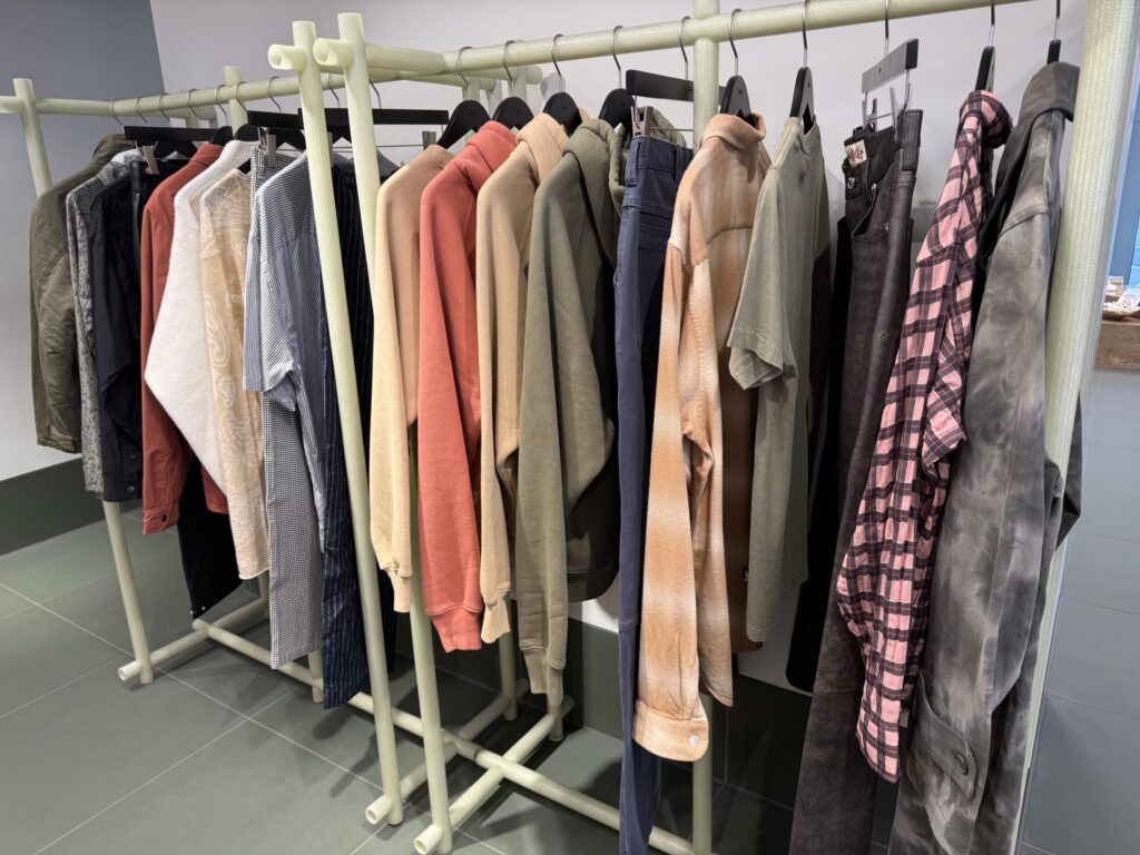 A view of a uniquely designed light green clothing rack holding a variety of archive items such as shirts, hoodies, and jackets in various colors and materials.