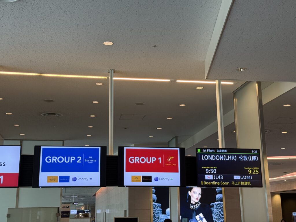 空港の搭乗ゲートにある案内ディスプレイ。JALのロンドン行きフライトの、グループ1(ファーストクラス)とグループ2(ビジネスクラス)の優先搭乗情報が表示されている。
