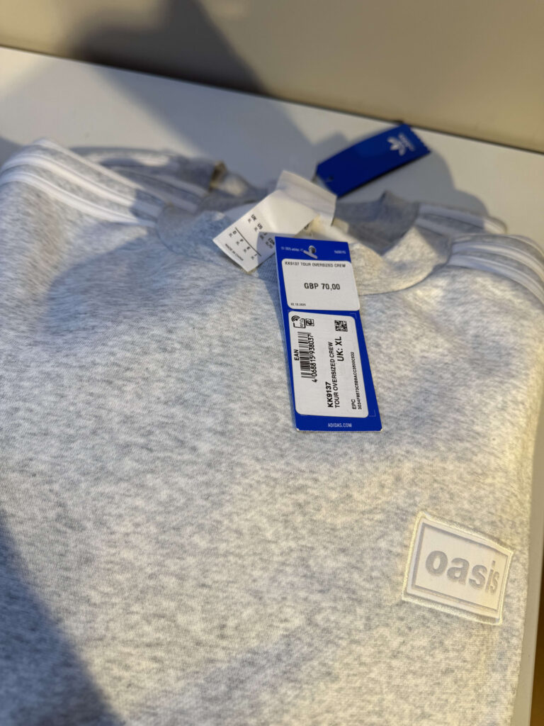 A folded grey adidas x Oasis collaboration sweatshirt with price tags attached, one showing a price of GBP 70.00.