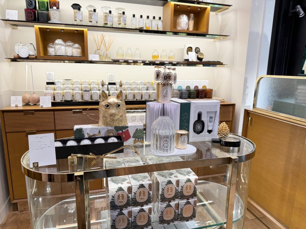 The interior of a Diptyque fragrance store. Holiday collection items such as candles and gift sets are arranged on shelves and a central glass display table.