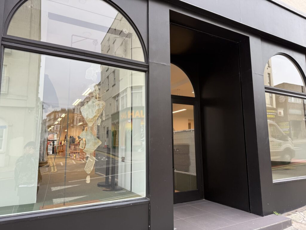 The exterior of a modern shop featuring a matte black facade. A large arched window reflects the buildings and sky of the street opposite. To the right is a recessed entrance.
