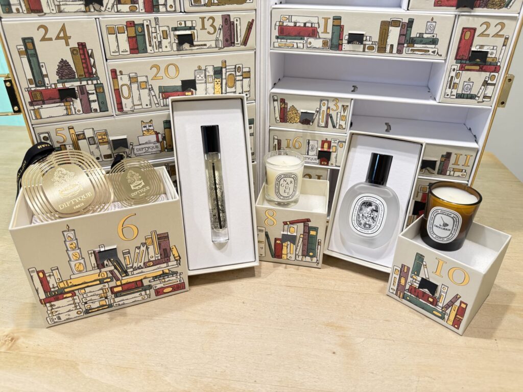diptyqueのアドベントカレンダーの6日目から10日目までの開封済みアイテム。香水、キャンドル、オーナメントが木製のテーブルの上に並んでいる。