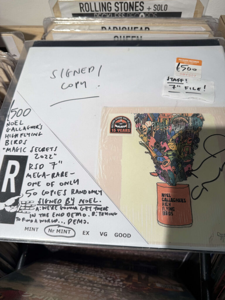 A signed, limited edition 7-inch record by Noel Gallagher's High Flying Birds, displayed in a record store rack with a £500 price tag.