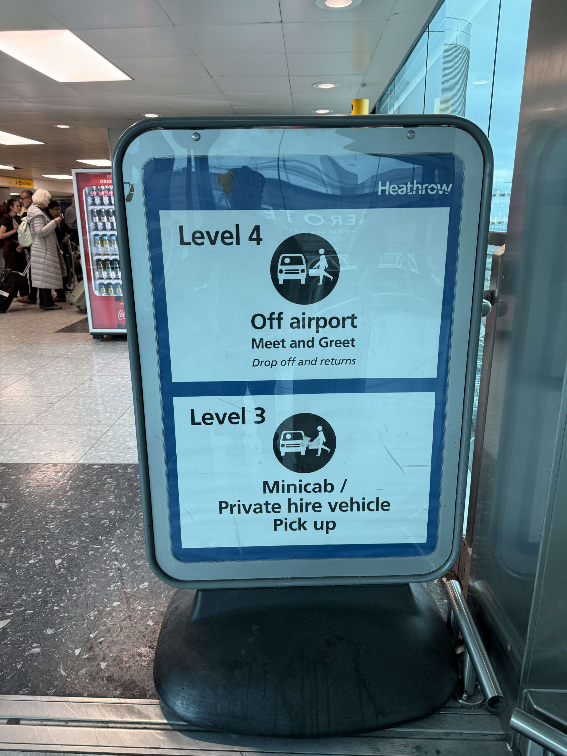 A sign inside Heathrow Airport indicating vehicle service levels. Level 4 is for 'Off airport Meet and Greet', and Level 3 is for 'Minicab / Private hire vehicle Pick up'.