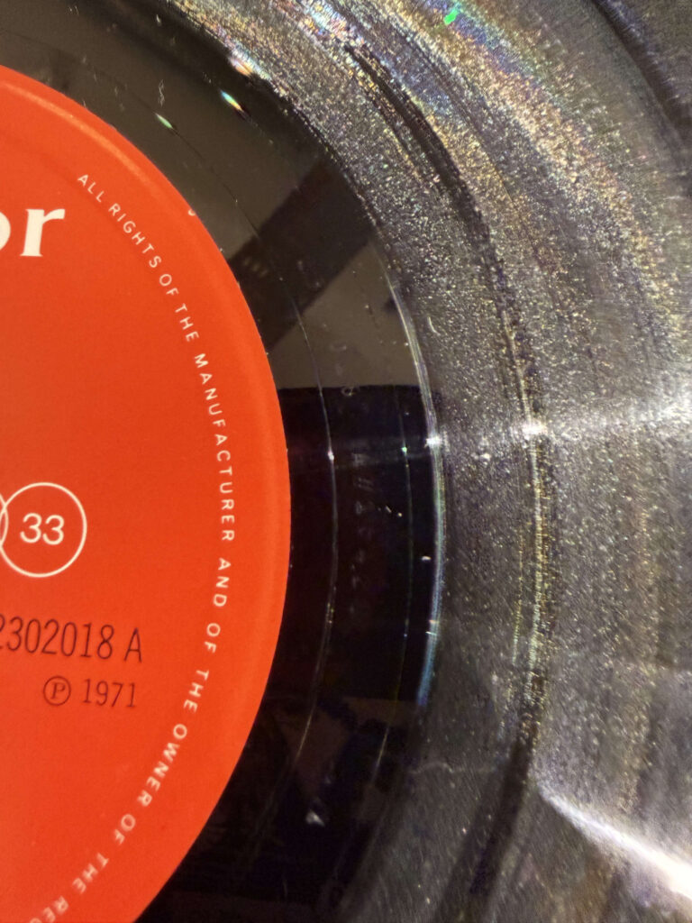 オレンジ色のレーベルと、光を反射して虹色に輝く黒い盤面が写ったレコード盤のクローズアップ。