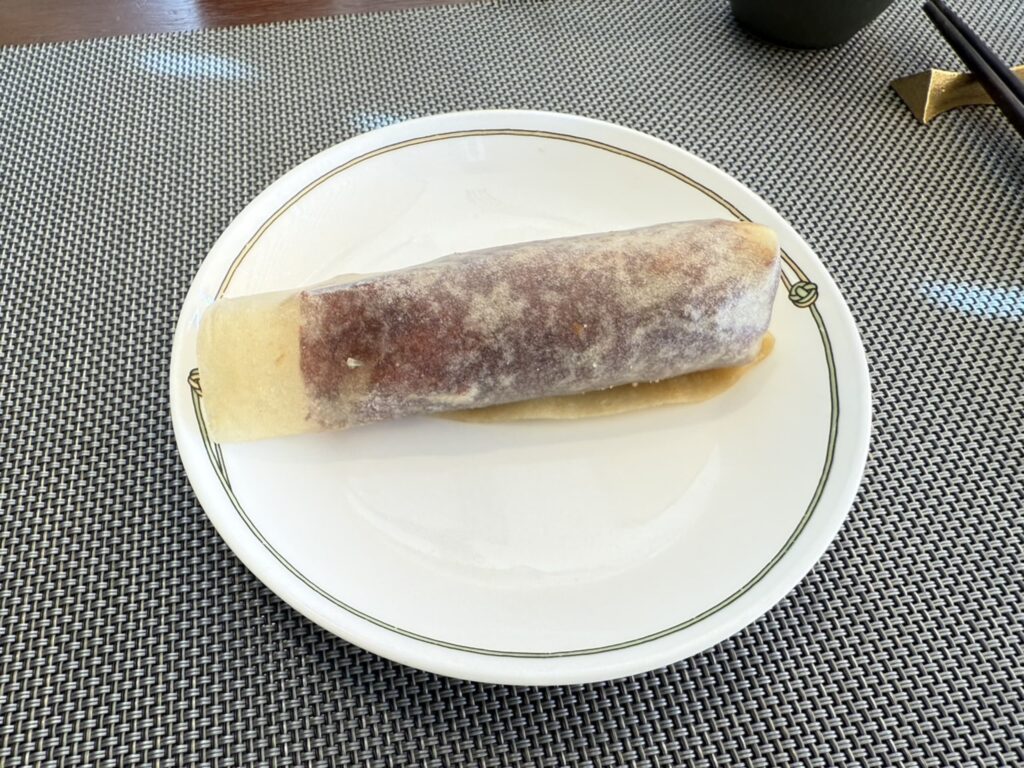 A single Peking duck wrap is placed on a white plate, which sits on a grey placemat.