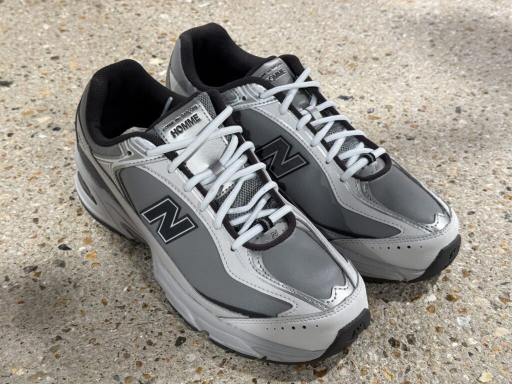 Grey and silver COMME des GARÇONS HOMME x New Balance U509 sneakers placed on a speckled concrete surface