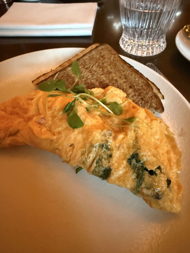 A fluffy omelet filled with greens and topped with fresh sprouts, served with a slice of toast on a white plate
