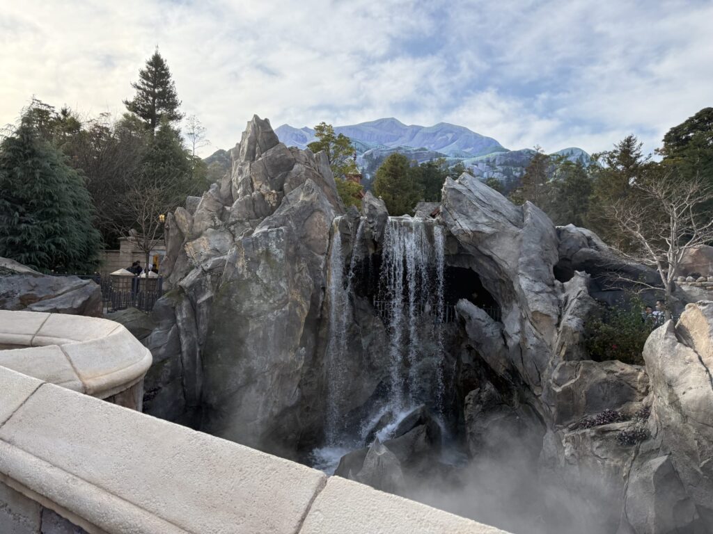 東京ディズニーランド「美女と野獣」エリアにある岩場と滝、背景に描かれた山脈の風景