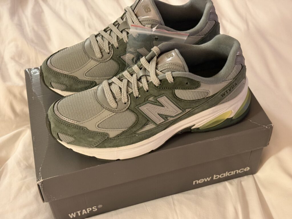 Olive and grey WTAPS collaboration sneakers sitting on top of a New Balance shoebox