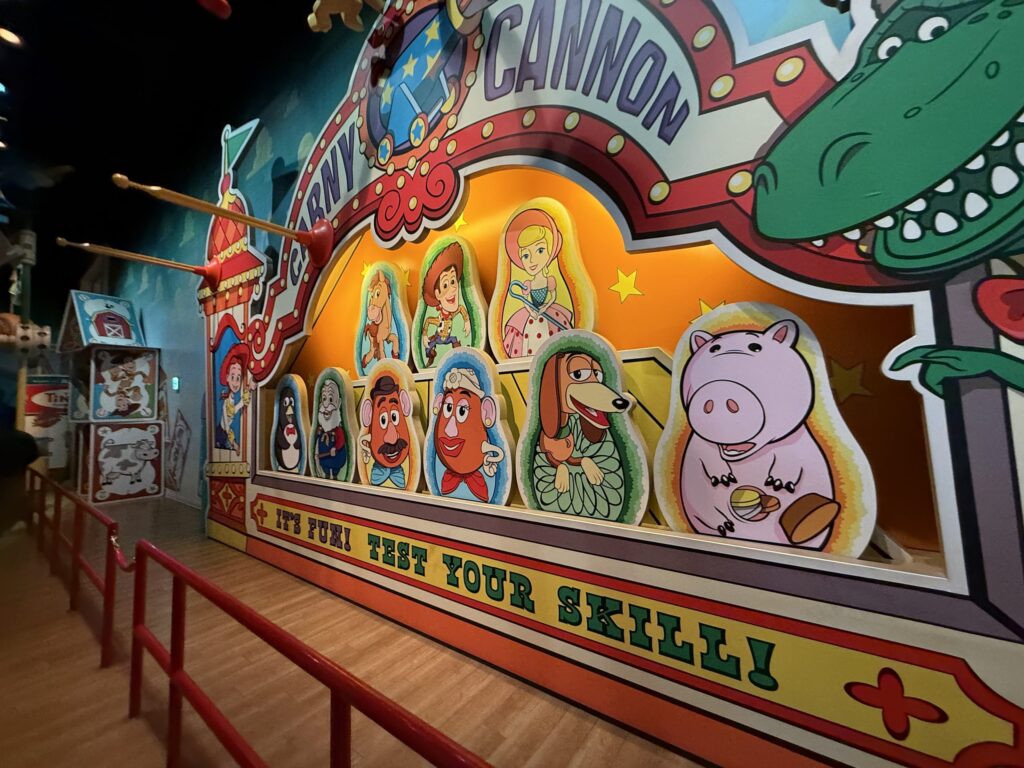 Colorful wall display in the Toy Story Mania queue featuring characters like Woody and Hamm designed as nesting dolls under a Carny Cannon sign