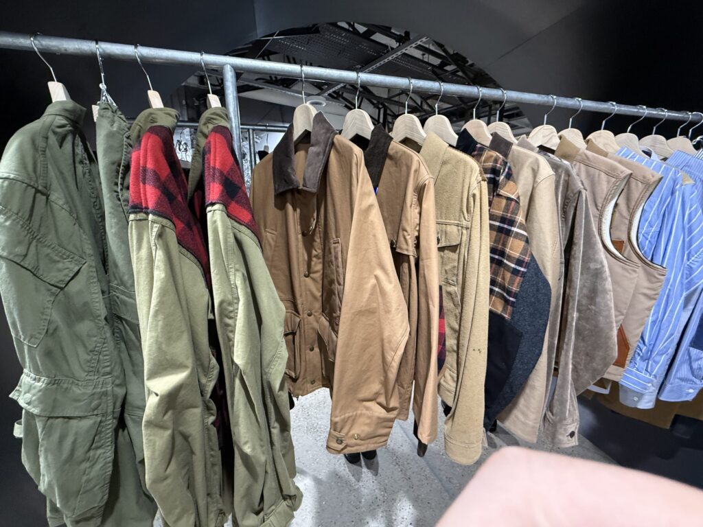 Clothing rack displaying Junya Watanabe and Filson collaboration jackets with red buffalo check accents alongside other outerwear