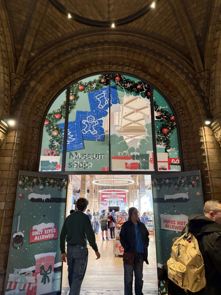 クリスマス装飾が施された自然史博物館のミュージアムショップのアーチ型入り口と、出入りする人々
