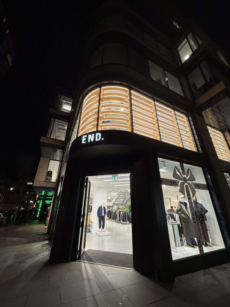 ロンドンのセレクトショップ「END.」の夜の外観。曲線的なガラス張りの建物とライトアップされたショーウィンドウ。