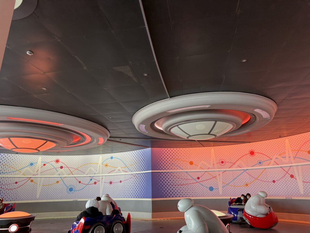 東京ディズニーランドのアトラクション「ベイマックスのハッピーライド」。未来的な円形の天井照明と、カラフルな波形模様の壁、そしてゲストを乗せたベイマックス型のライド。
