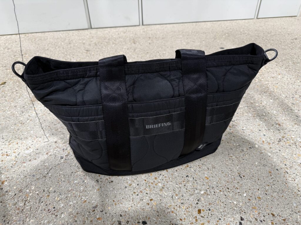 Black nylon ripstop quilted tote bag from the COMME des GARÇONS HOMME x BRIEFING collaboration sitting on concrete ground
