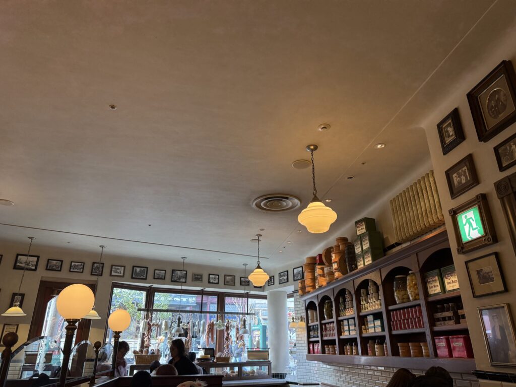 Interior view of a New York style deli featuring high ceilings, warm pendant lighting, and shelves stocked with vintage tins and jars