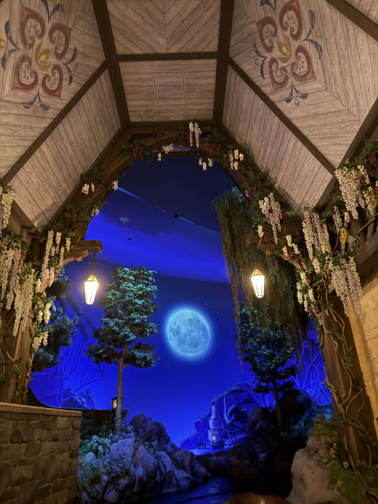 A wooden archway decorated with flowers and lanterns framing a large full moon in a dark blue night sky