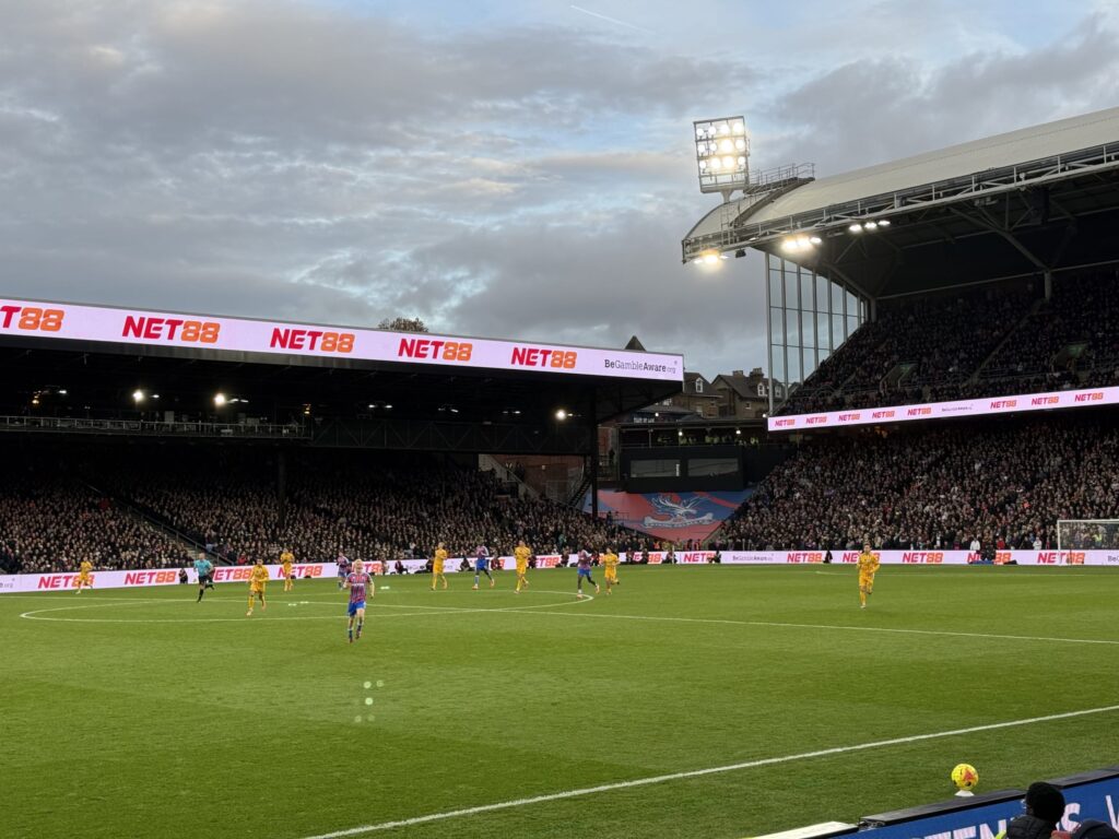 Soccer stadium illuminated by floodlights at dusk with players on the field and packed stands