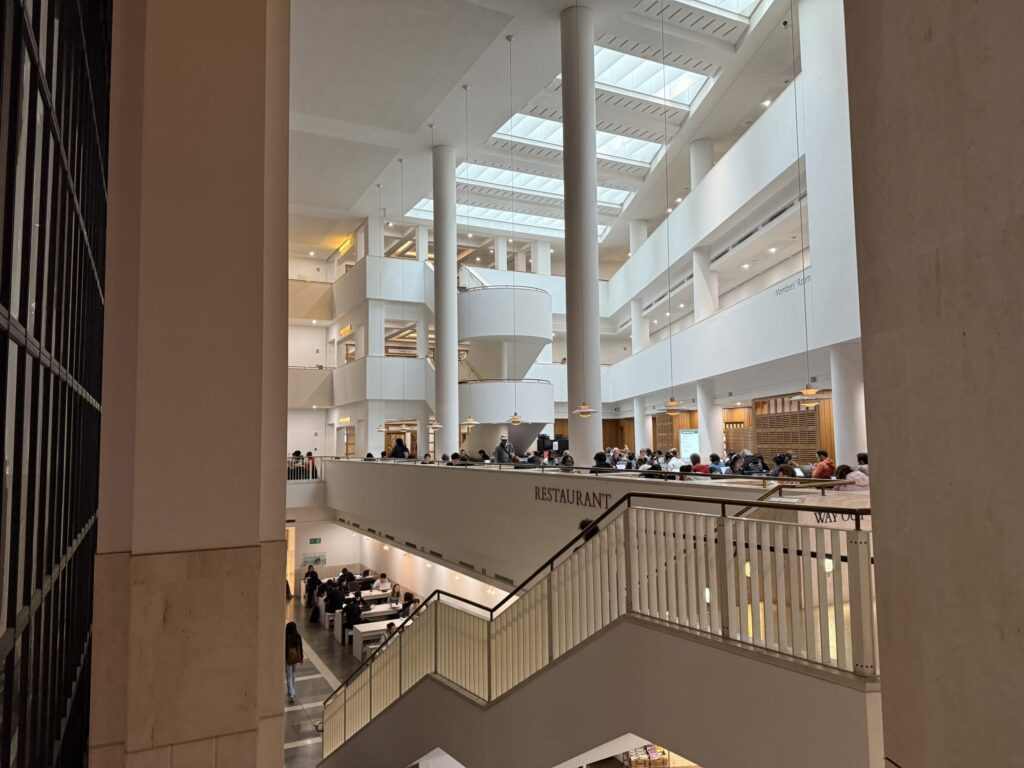 白い柱と天窓がある開放的な図書館の吹き抜けで、多くの人がテーブルで作業をしている様子