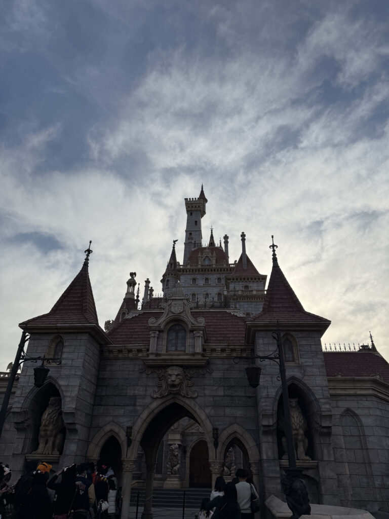 Exterior view of the Beauty and the Beast Castle towering against a cloudy sky with lion statues at the entrance