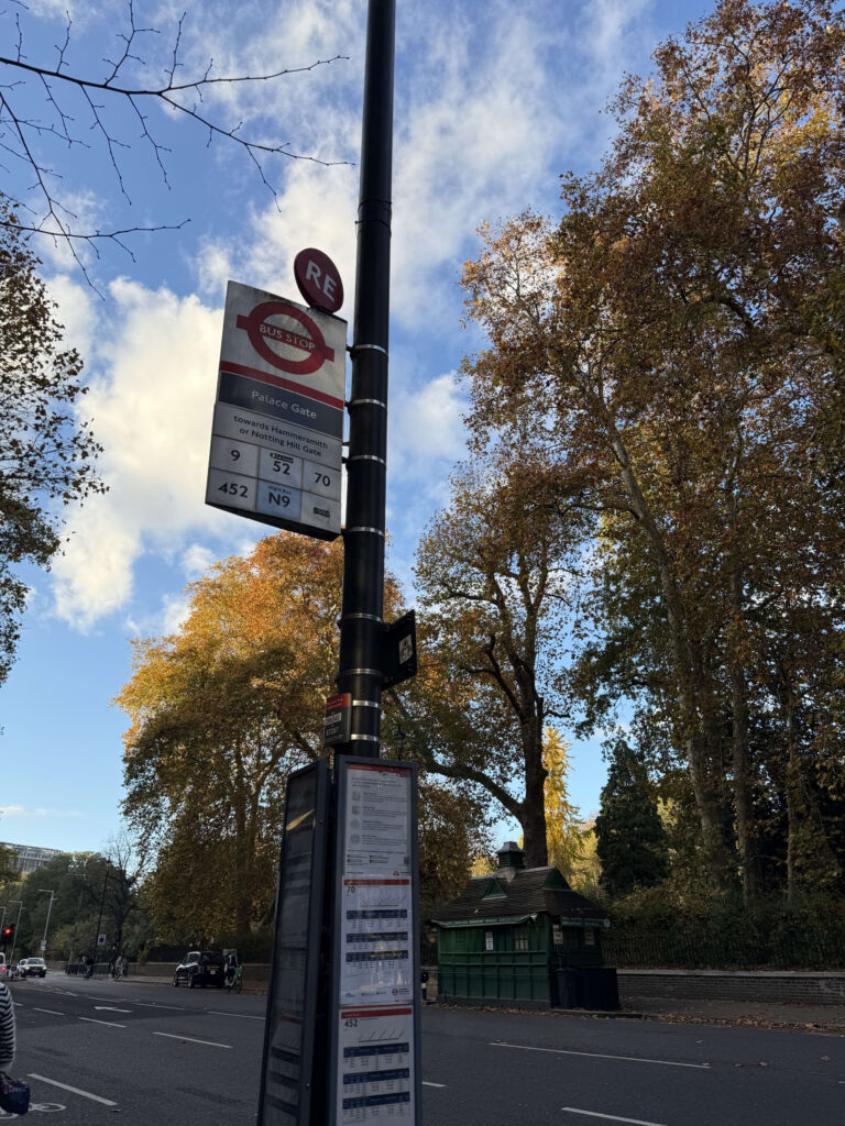 秋のロンドンにあるパレス・ゲートのバス停。紅葉した木々と青空を背景に、バス停の標識が立っている。