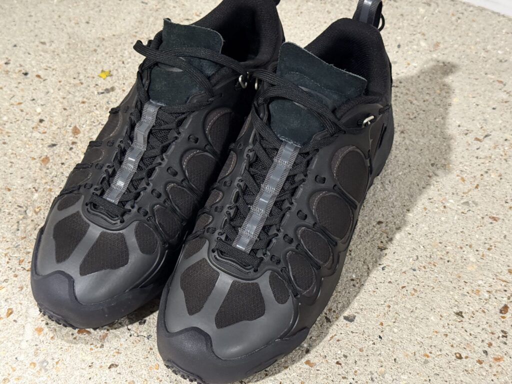 コンクリートの床に置かれたCOMME des GARCONS JUNYA WATANABE MAN × OAKLEY FACTORY TEAMの黒いIBEXスニーカー