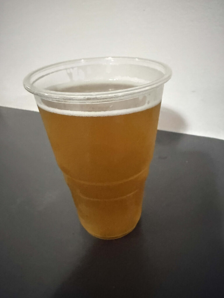 Palace Ale beer in a clear plastic cup sitting on a dark table