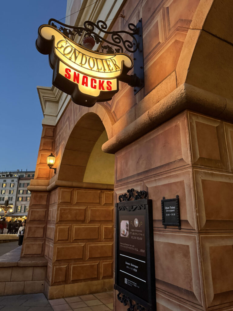 Illuminated Gondolier Snacks sign hanging on a textured wall against a twilight sky.