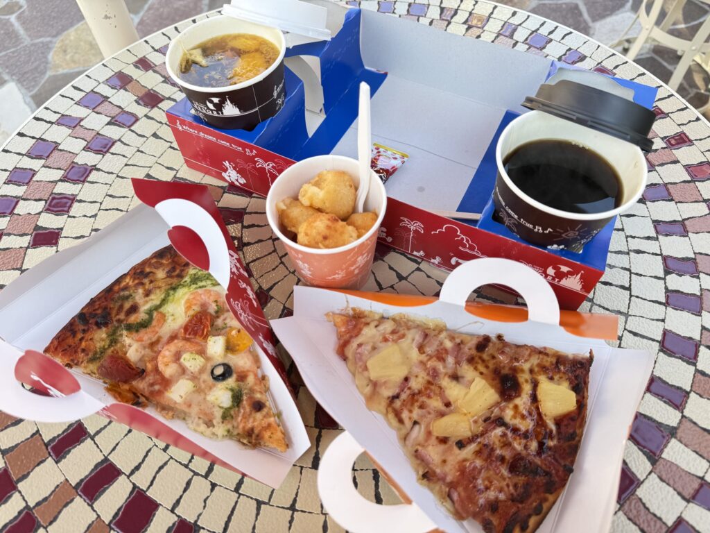 Seafood pizza, pineapple pizza, potato nuggets, hot fruit tea, and coffee on a mosaic tile table